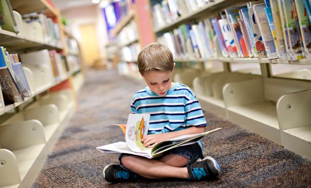 Child reading book sitting on floor in library