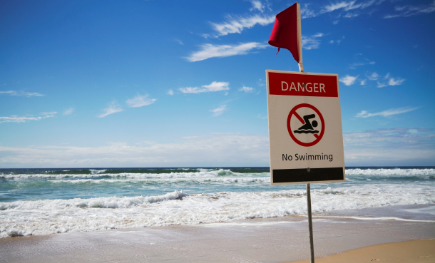 Shoreline at beach with sign that says 