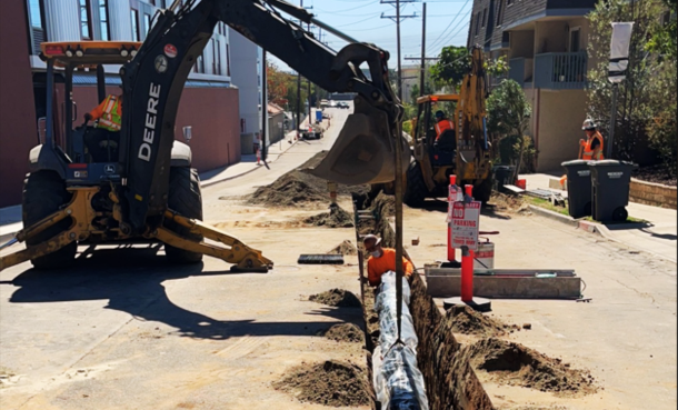 Construction workers with an excavator and open trench pipe